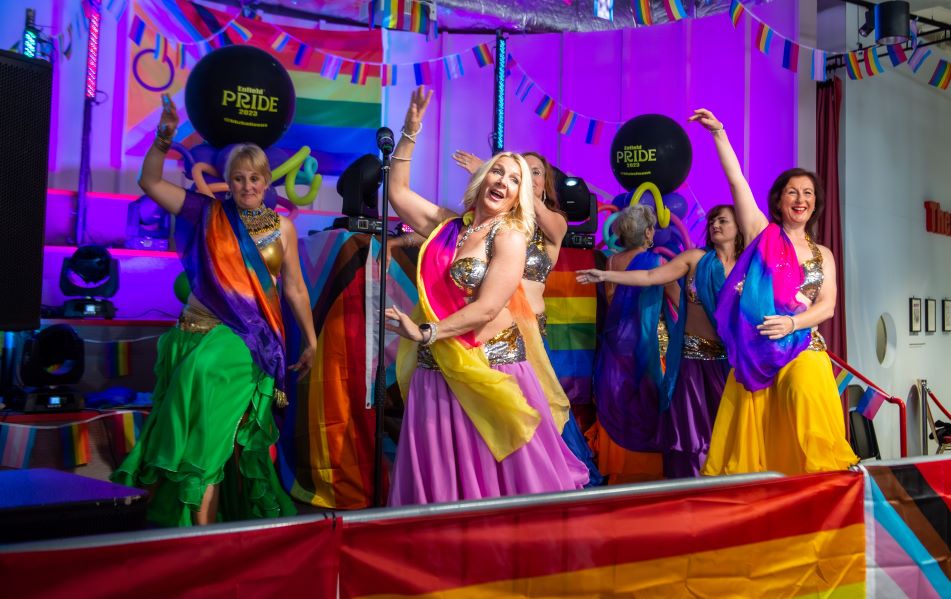 Vibrant dancers in colorful costumes at Dugdale Arts Centre pride event.