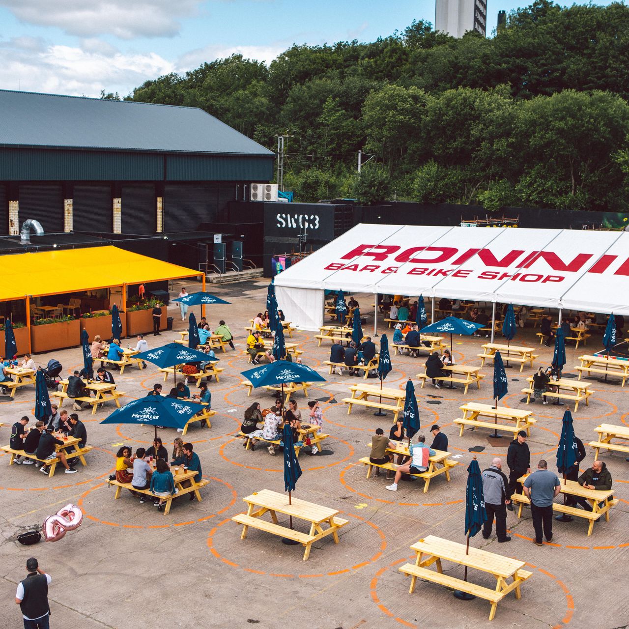 Vibrant outdoor event space with tent and picnic seating at SWG3 for gatherings and networking.