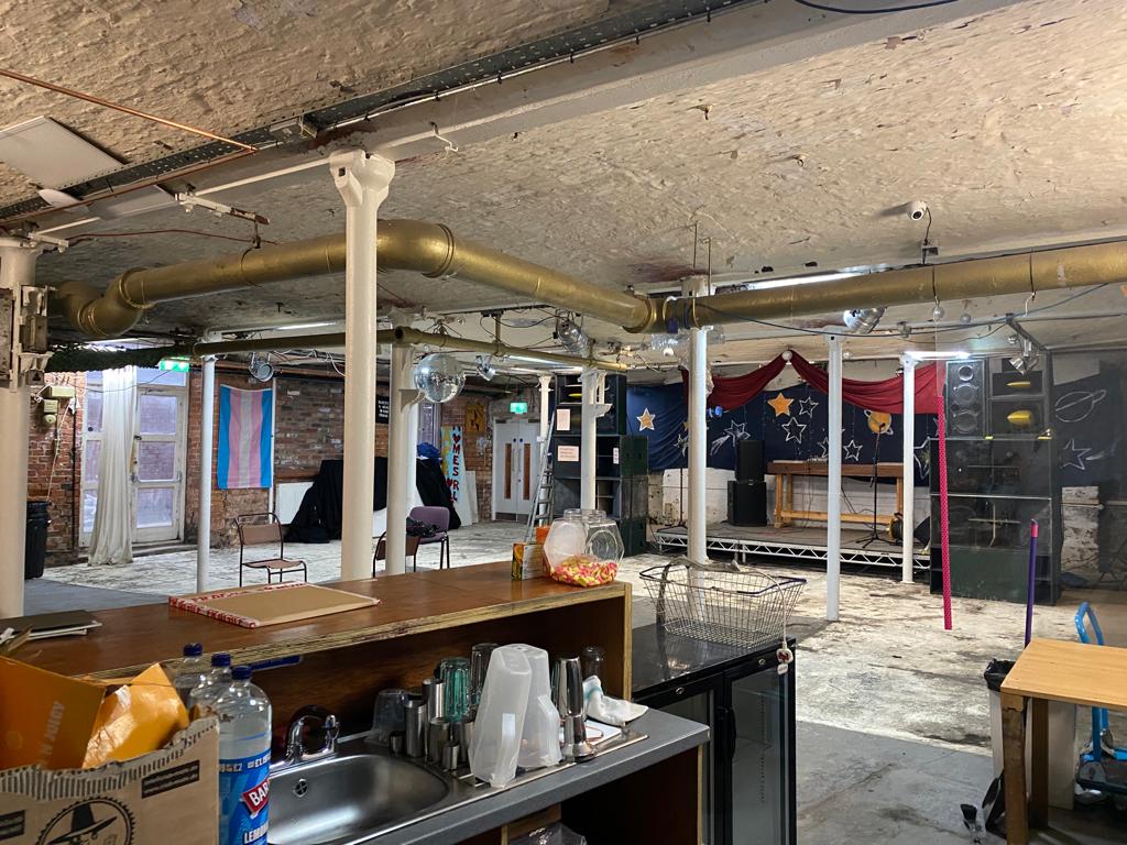 Versatile industrial event space with stage and bar for performances and gatherings.