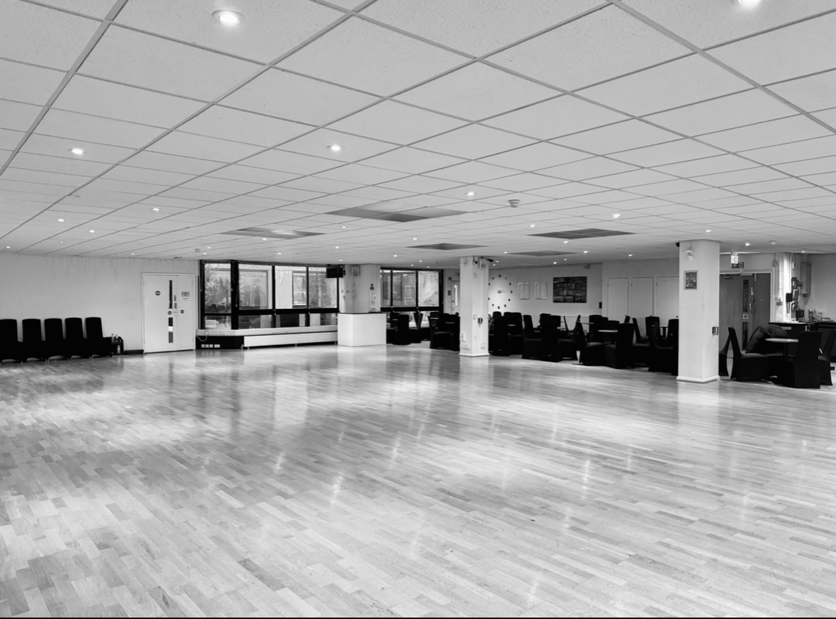 Spacious event space with polished wooden floors, ideal for meetings and workshops.