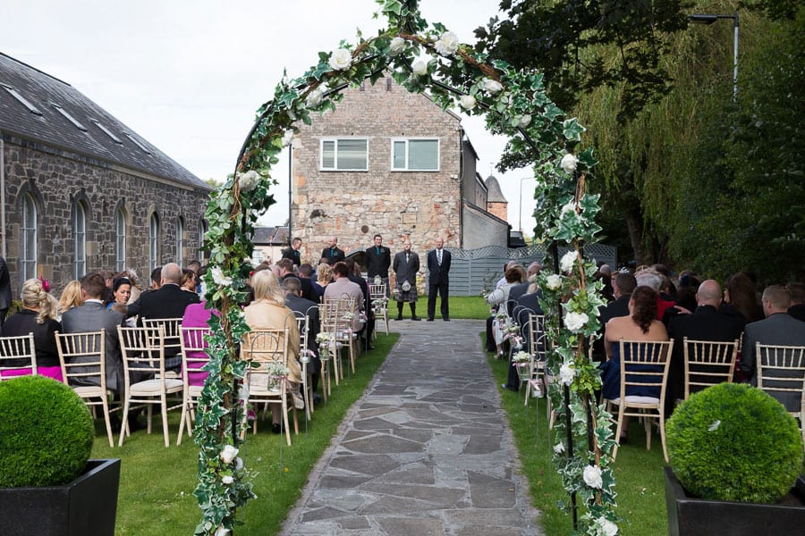 Outdoor wedding ceremony at Eskmills Venue with floral archway and lush greenery.