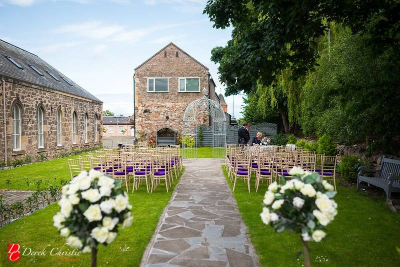 Outdoor wedding ceremony at The Cellars in Eskmills, featuring lush greenery and rustic stone.