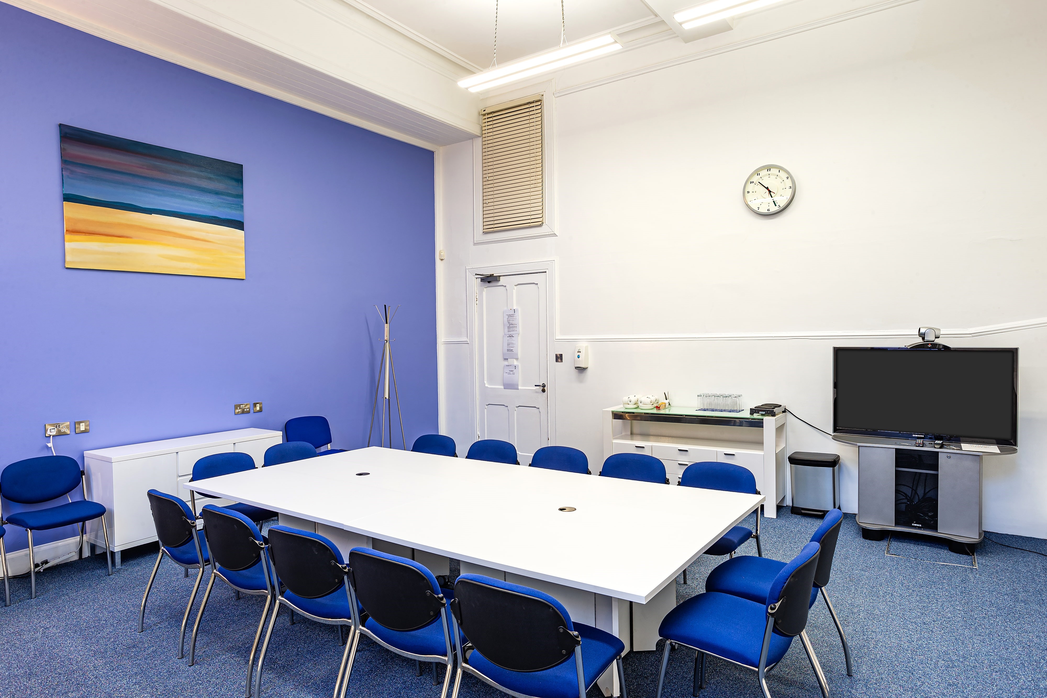 Interview room with large white table and blue chairs, perfect for workshops and meetings.