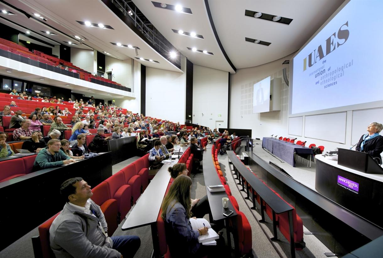 Modern conference in tiered seating auditorium with engaged speaker and attentive audience.