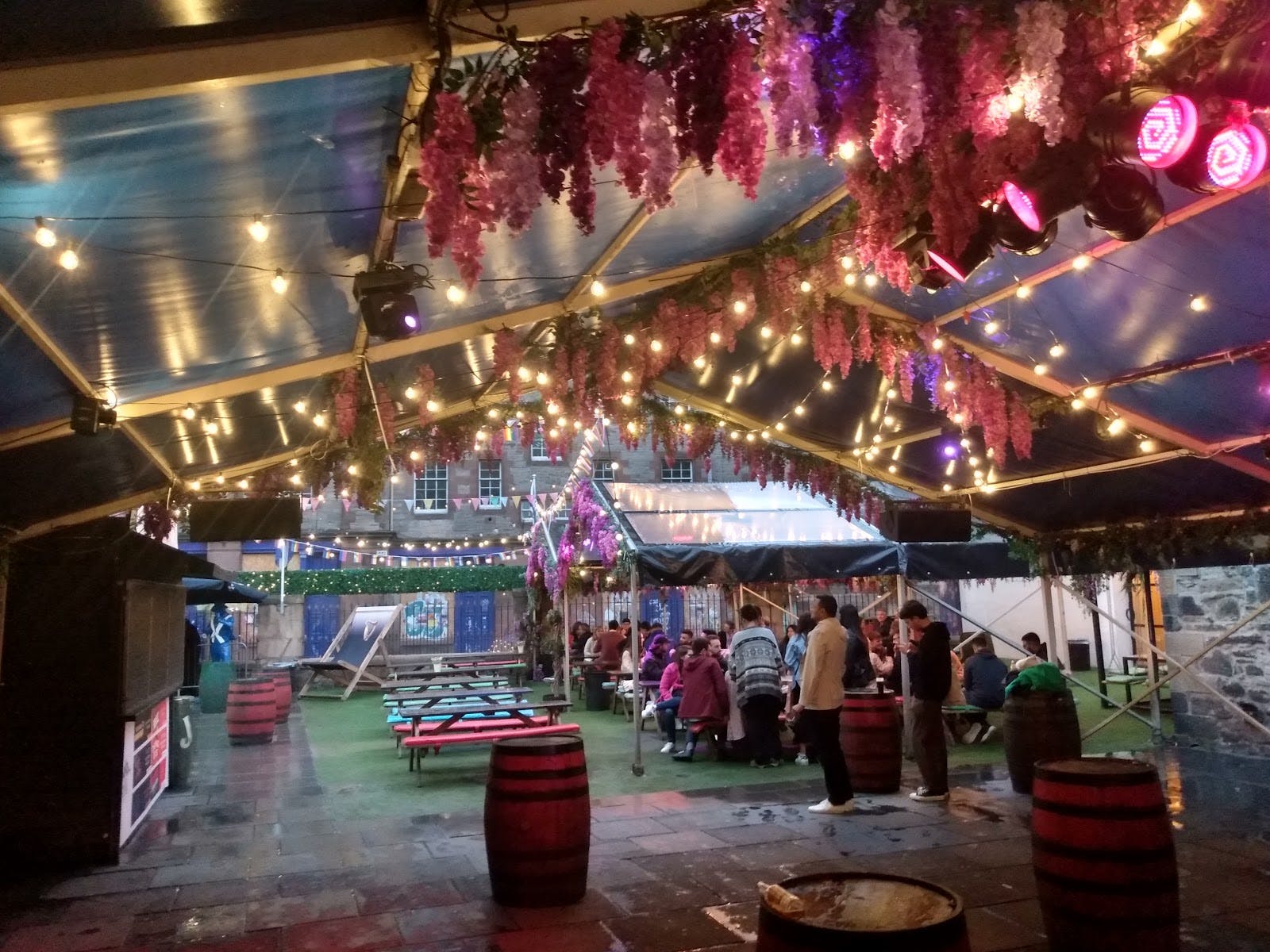 Vibrant outdoor event space at The Three Sisters Bar with hanging flowers and string lights.