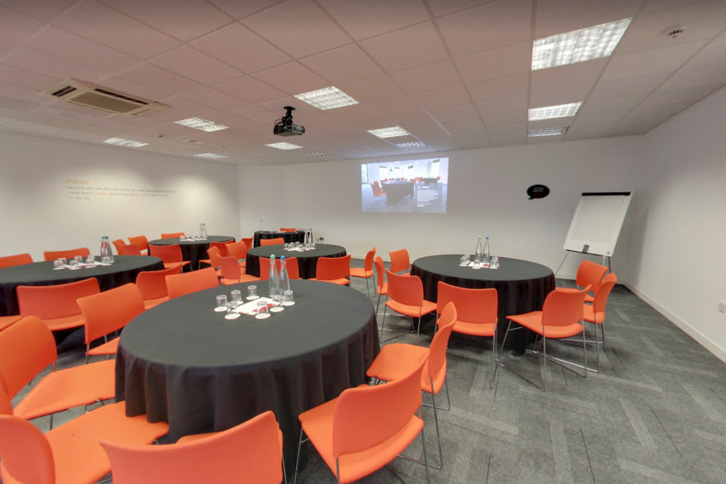 Modern meeting room in The Studio Leeds, featuring round tables and vibrant orange chairs.