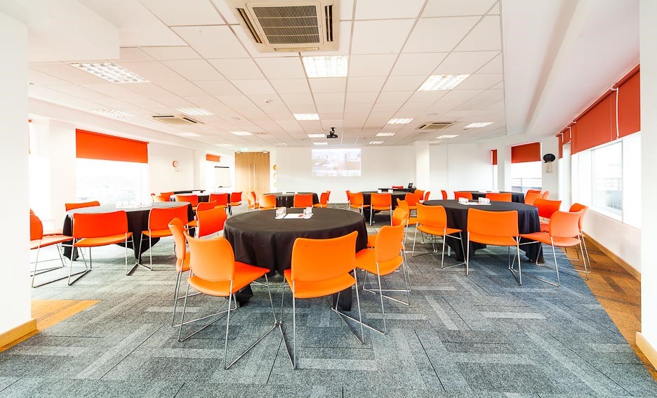 Modern conference center with round tables and orange chairs, perfect for workshops and networking.