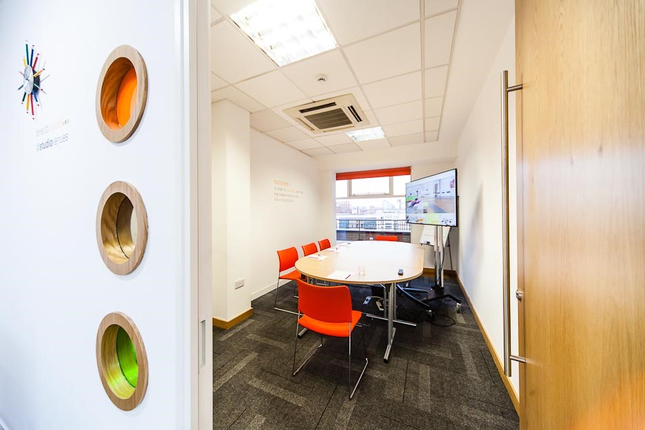 Modern meeting room in The Studio Leeds with round table and bright orange chairs.