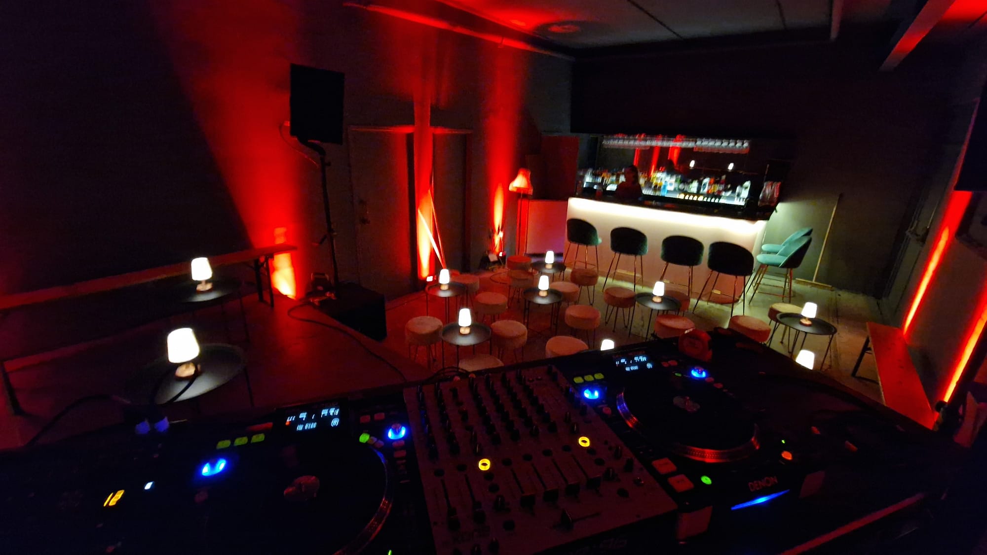 Stylish event space with DJ setup and red lighting, ideal for networking and celebrations.