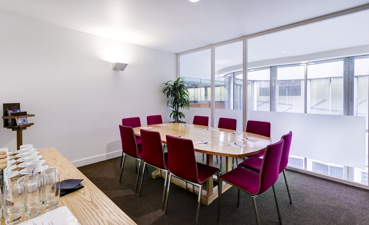 Modern meeting room with wooden table and red chairs, ideal for collaborative events.