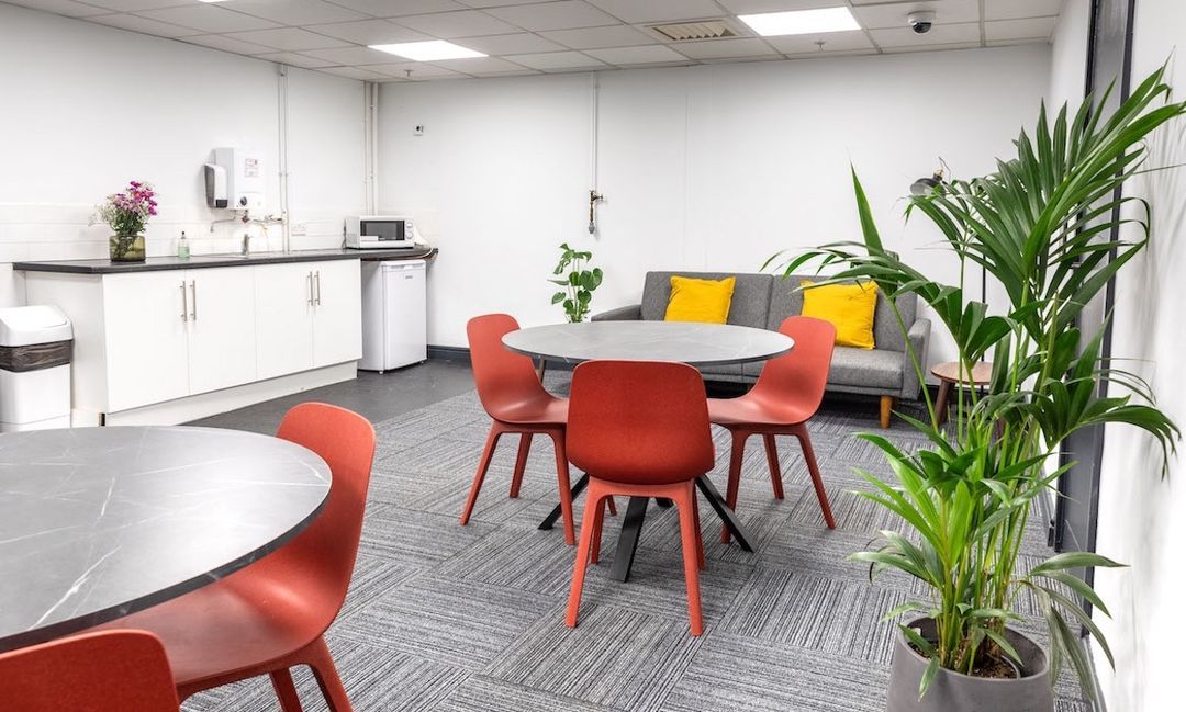 Modern break room with round tables and red chairs at Troubadour Brent Cross Studios.