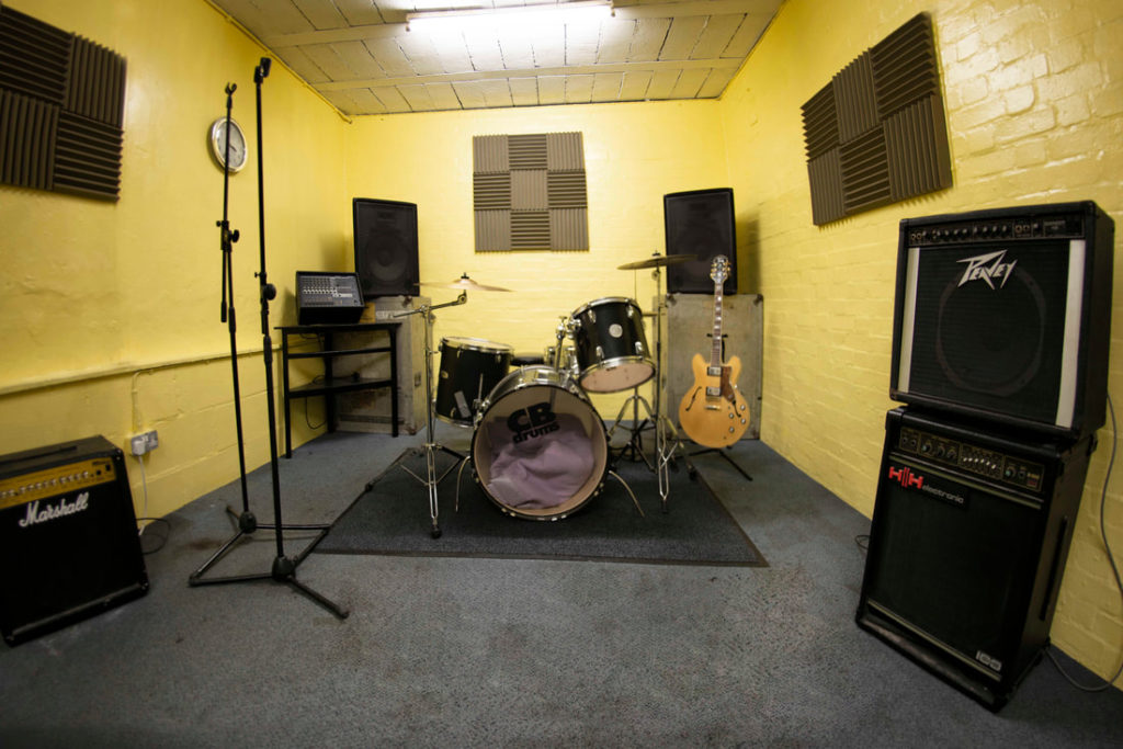 Rehearsal studio with drum set and vibrant yellow walls for music workshops and team-building.