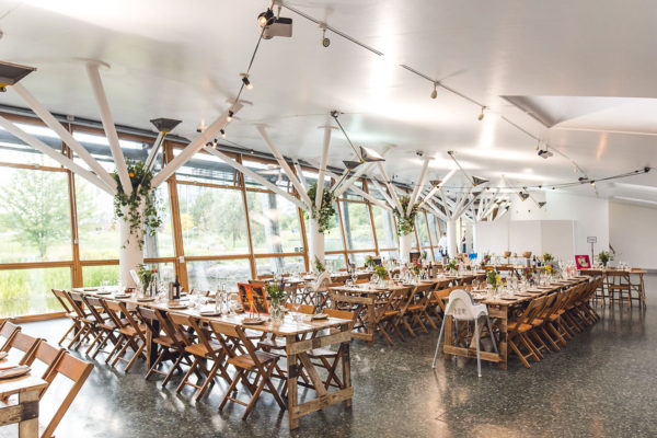 Contemporary glass-walled event space with wooden tables, ideal for weddings and corporate events.