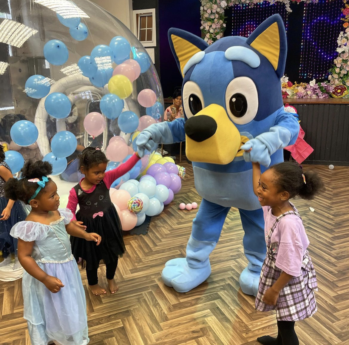 Children's event at Magdalen Hall with costumed character and colorful balloons.