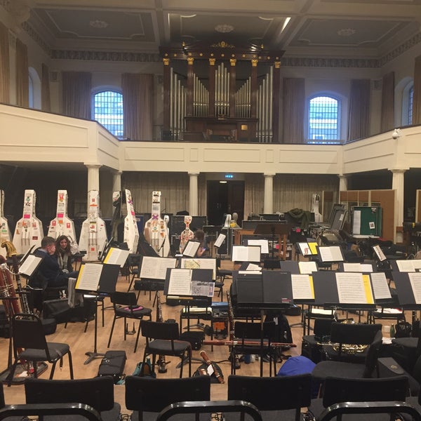 Orchestral rehearsal at Henry Wood Hall with music stands and string instruments.