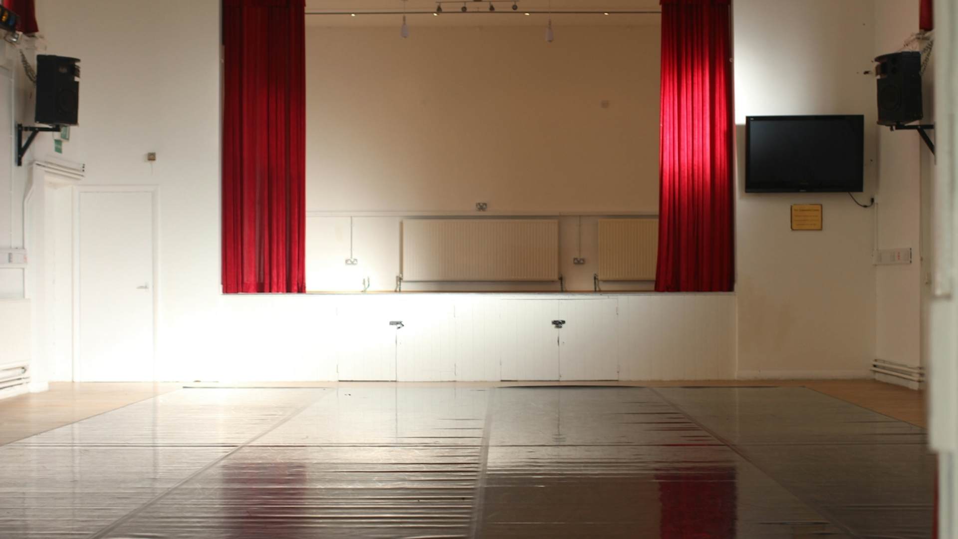 Versatile event space with polished floor and red curtains for meetings and performances.