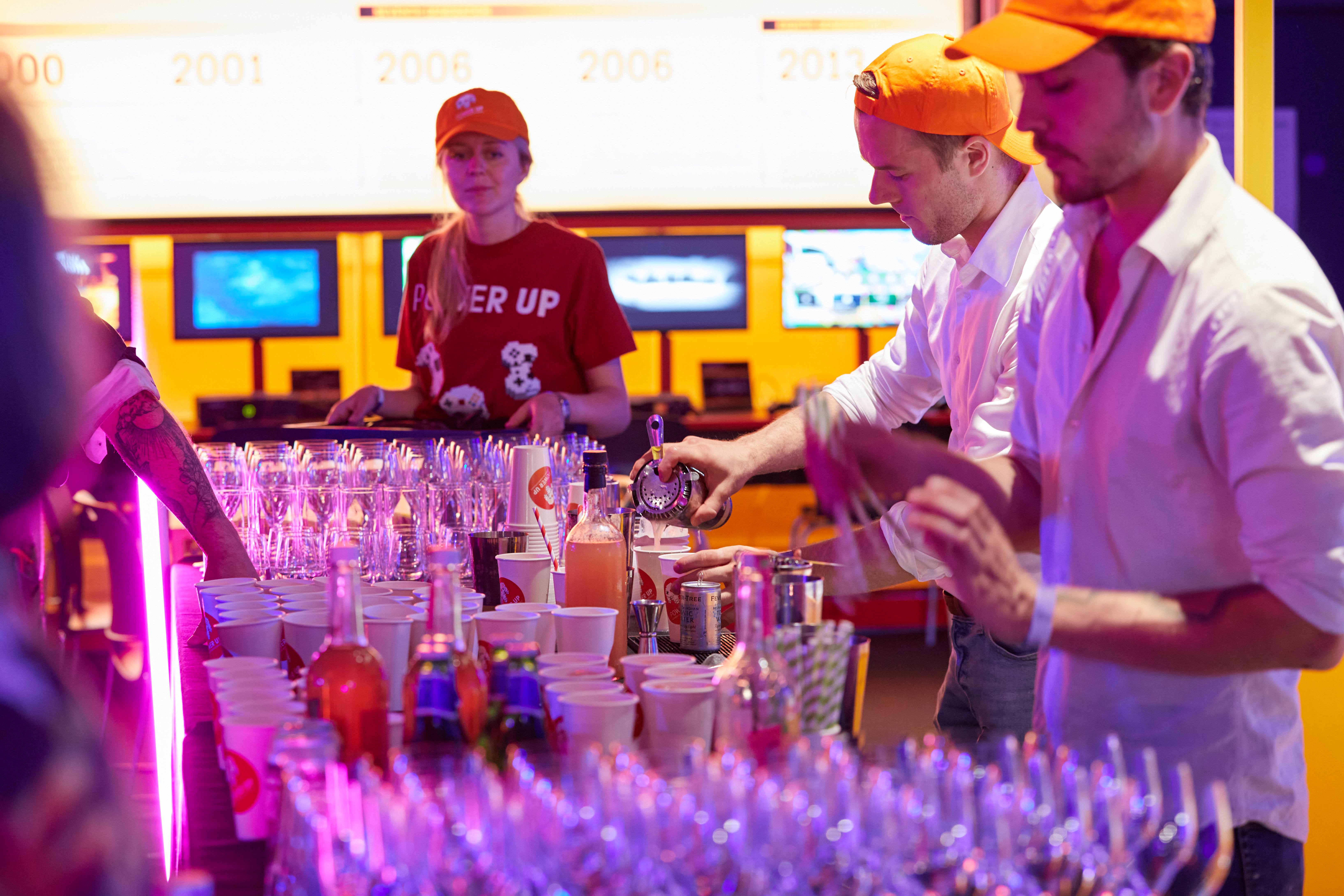 Vibrant event bar at Power Up, Science Museum with staff in orange caps preparing drinks.