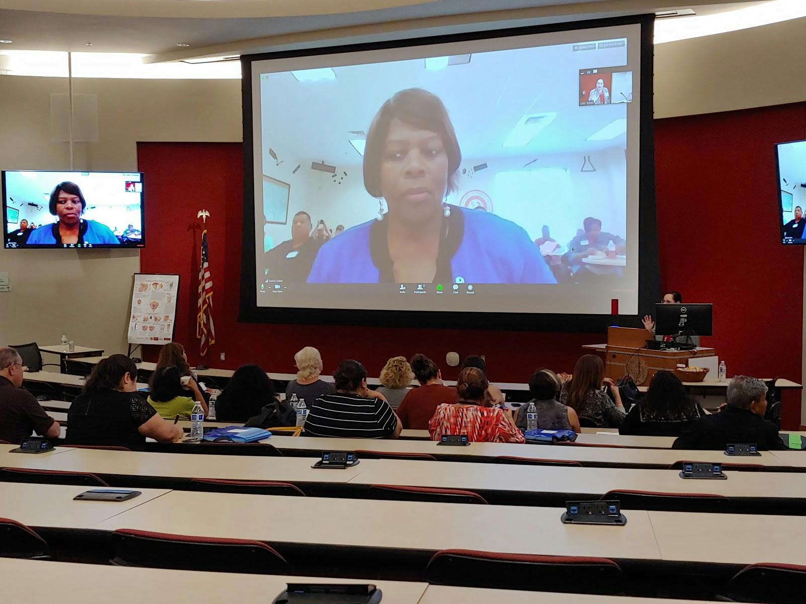 Hybrid meeting setup in Aresty Auditorium with large screen and engaged audience.