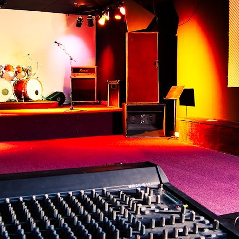Vibrant music rehearsal studio with stage, drum kit, and colorful lighting for events.