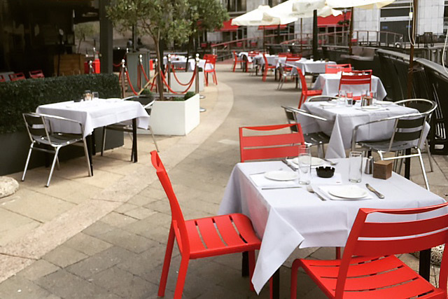Outdoor terrace dining area with white linens and red chairs, perfect for events and gatherings.