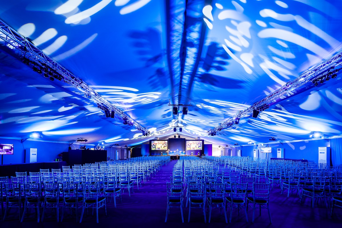 Spacious event tent with blue lighting, ready for a conference or presentation.