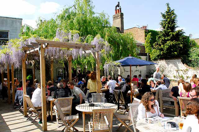 Vibrant beer garden at The Victoria with wisteria pergola, ideal for summer events.