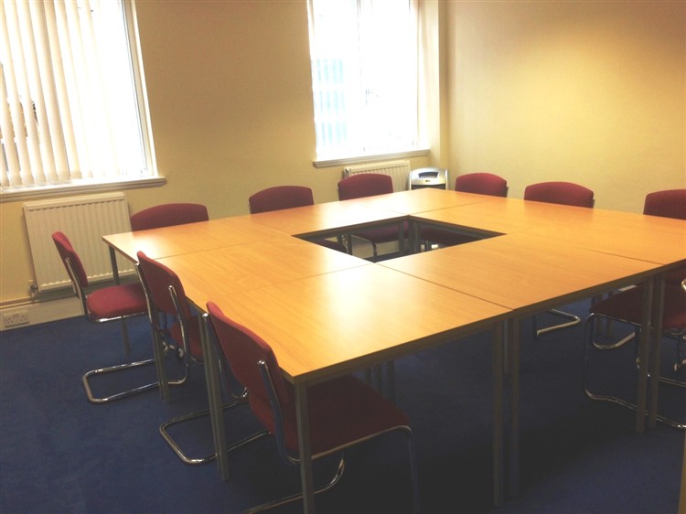 Meeting room with square table and red chairs for collaborative discussions at Christian Street Hub.