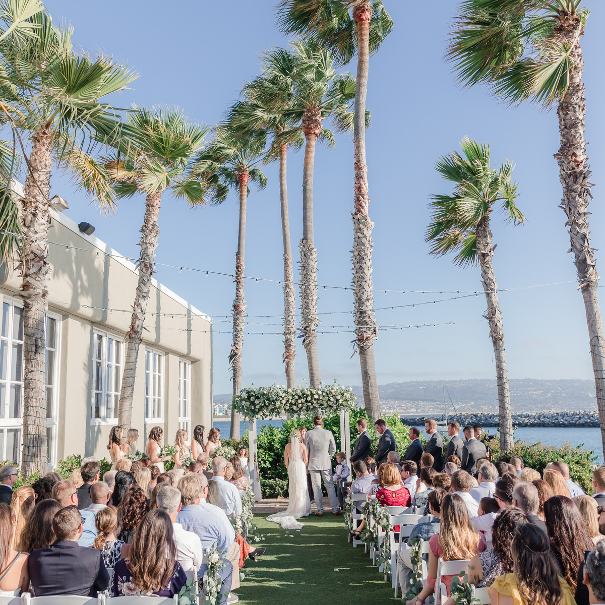 Outdoor wedding at Waterfront Ballrooms with floral arch and tropical backdrop.