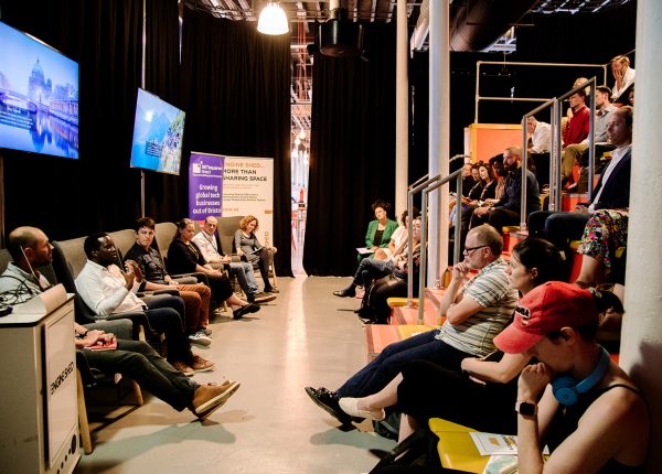 Dynamic panel discussion in modern event space with engaged audience and screens.