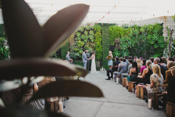 Outdoor wedding ceremony in Green Room at SmogShoppe with lush greenery and wooden seating.