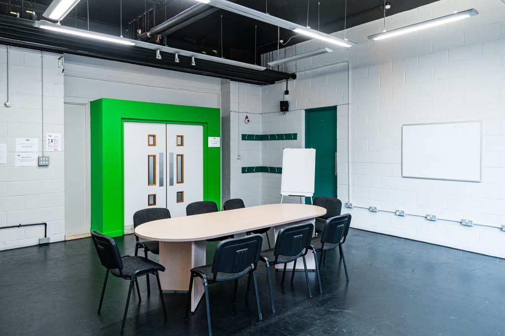 Versatile meeting space with round table and green accent wall for workshops and team meetings.