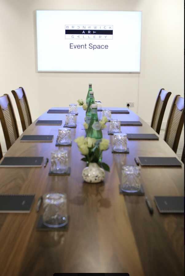 "Elegant meeting setup with wooden table and fresh flowers at Brunswick Art Gallery."