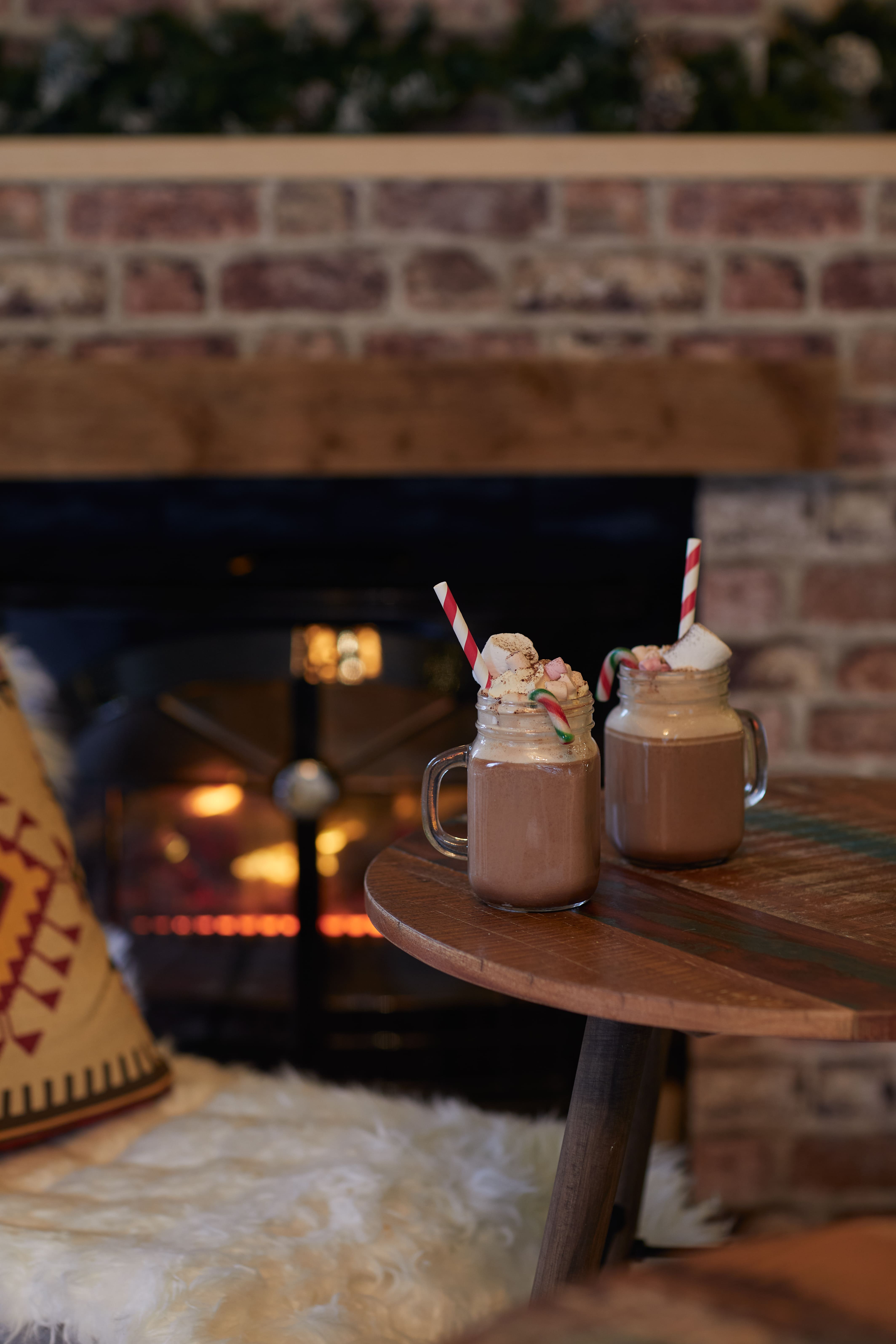 Festive hot chocolate mugs by a cozy fireplace for winter gatherings and holiday parties.