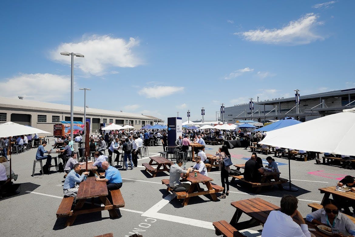Vibrant outdoor event space with picnic tables for networking under blue sky.