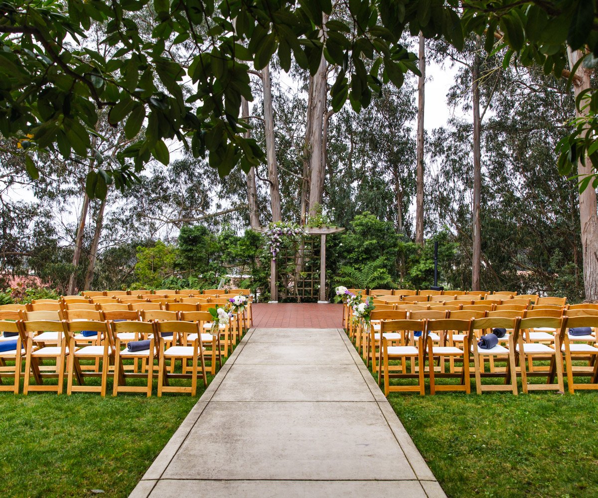 Outdoor garden ceremony space with wooden chairs and lush greenery, ideal for weddings.