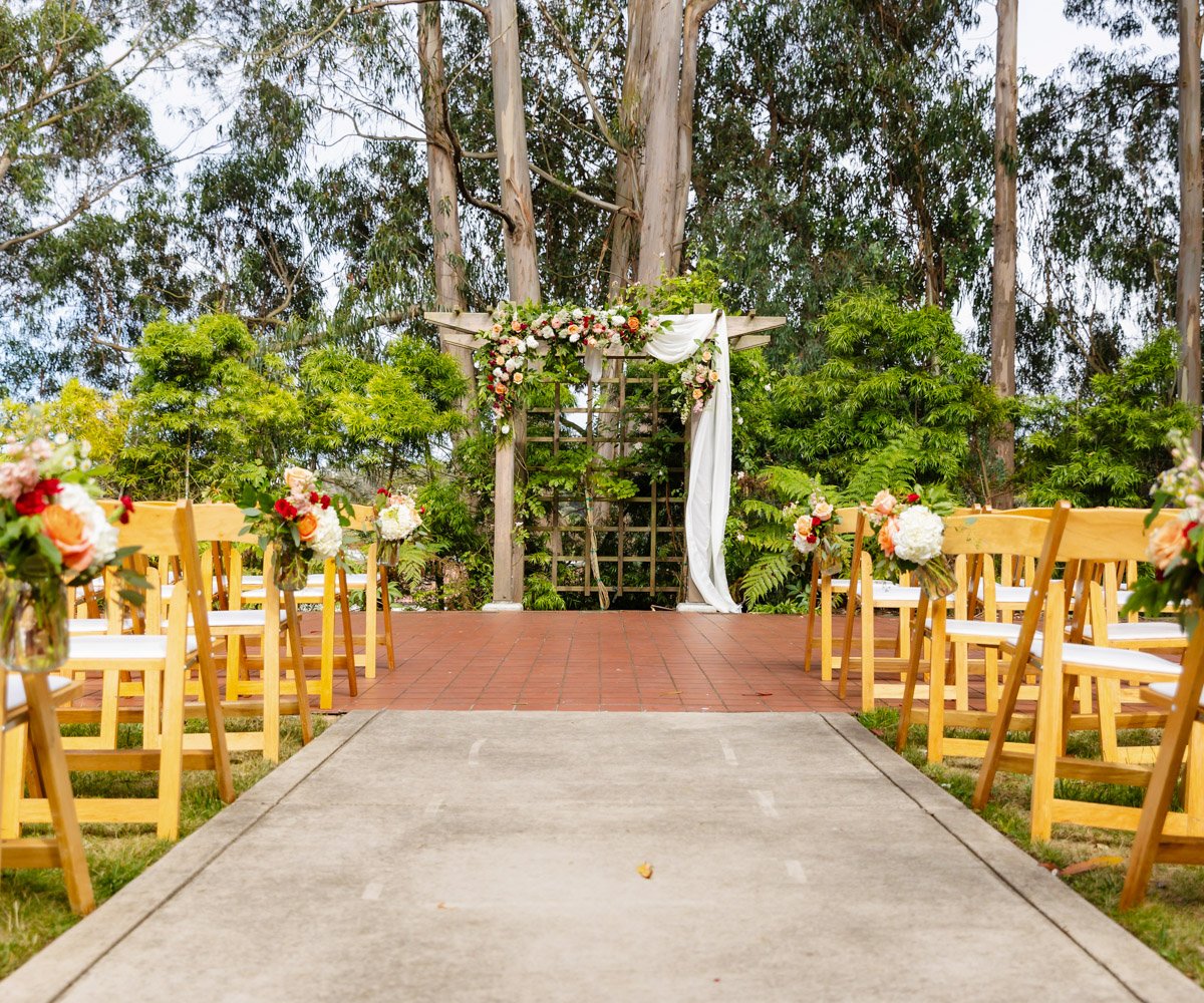 Outdoor wedding ceremony in Presidio Chapel with floral arch and wooden chairs.