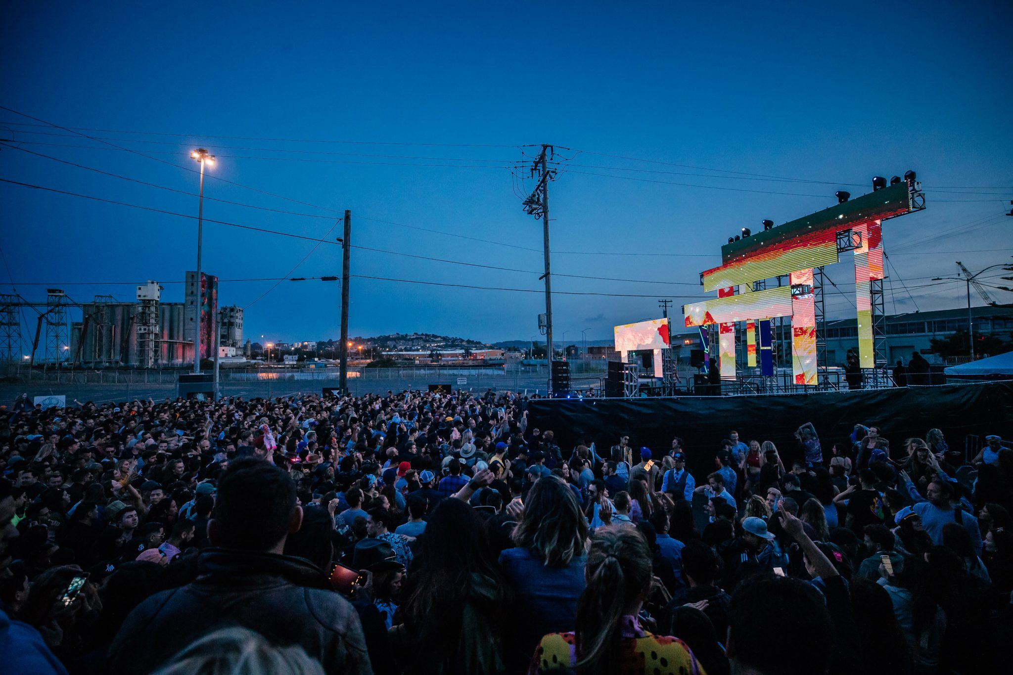 Vibrant Block Party at dusk with a large crowd enjoying a colorful stage performance.