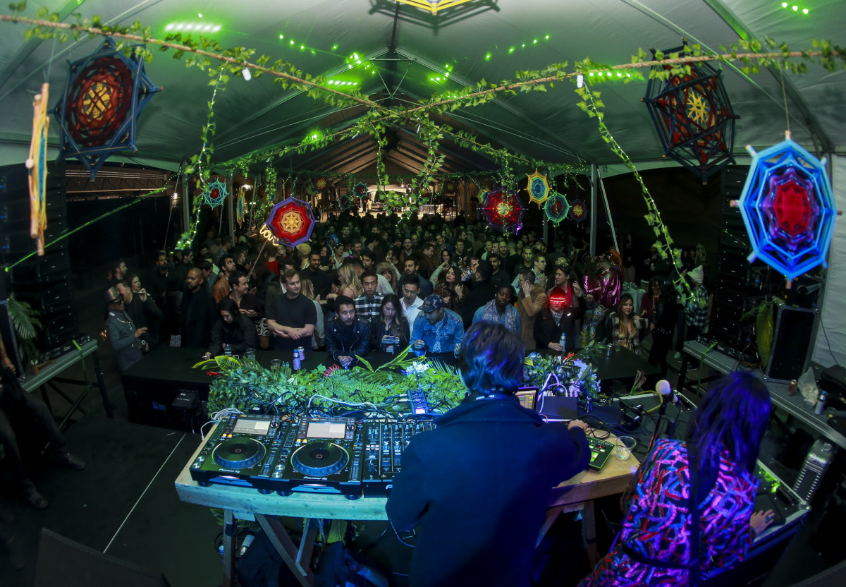 Vibrant Block Party in The Midway with DJ, colorful lights, and lush greenery.