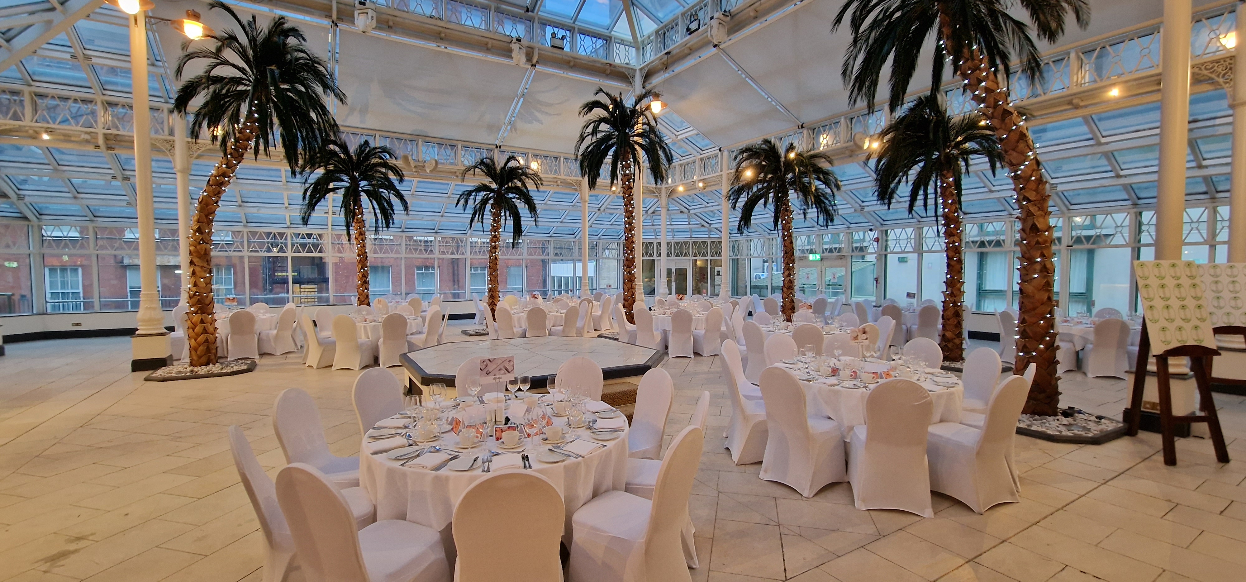 Elegant event space with round tables and palm trees at Millennium Gloucester, ideal for weddings.