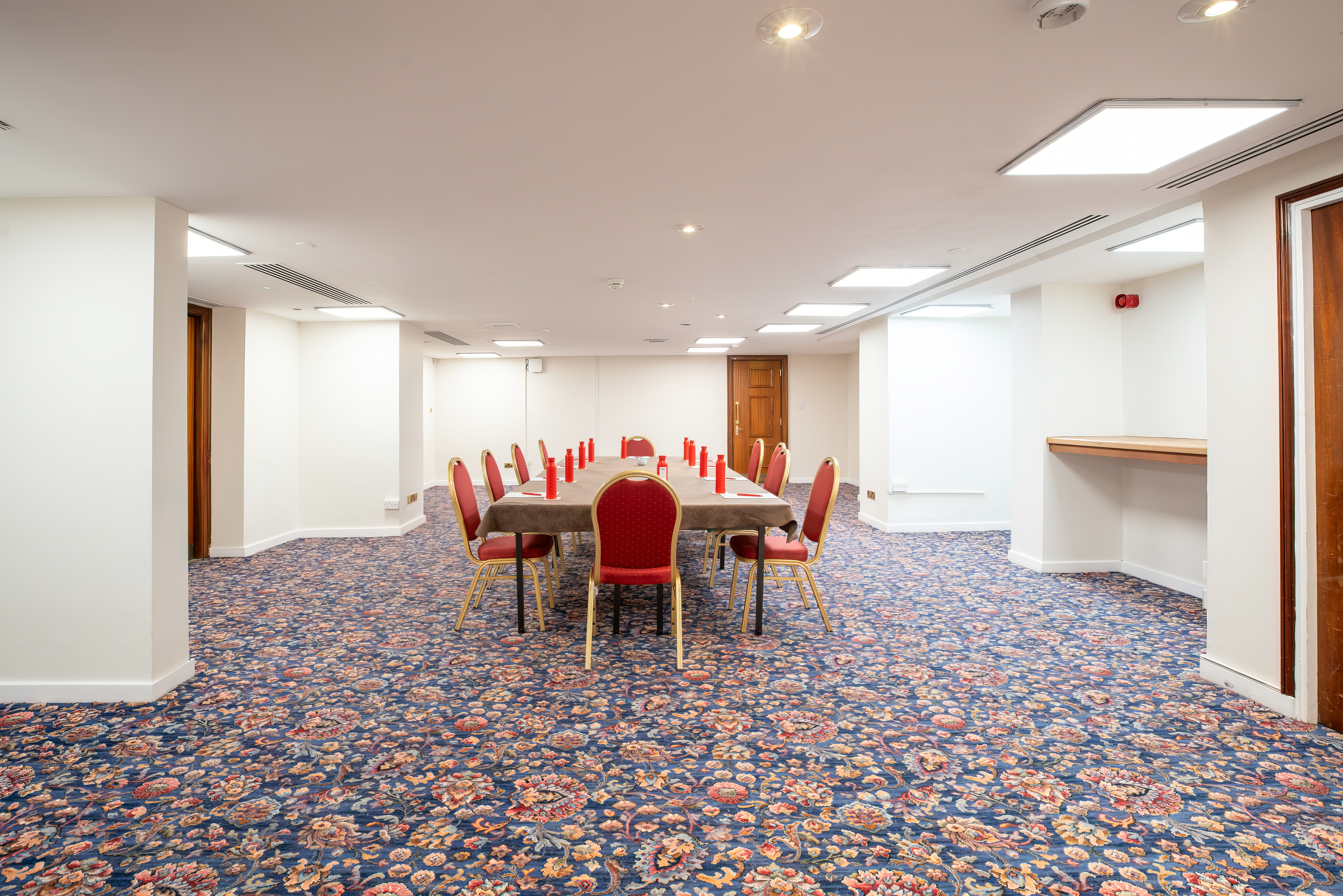 Versatile meeting room with long table and red chairs for workshops in Kensington, London.