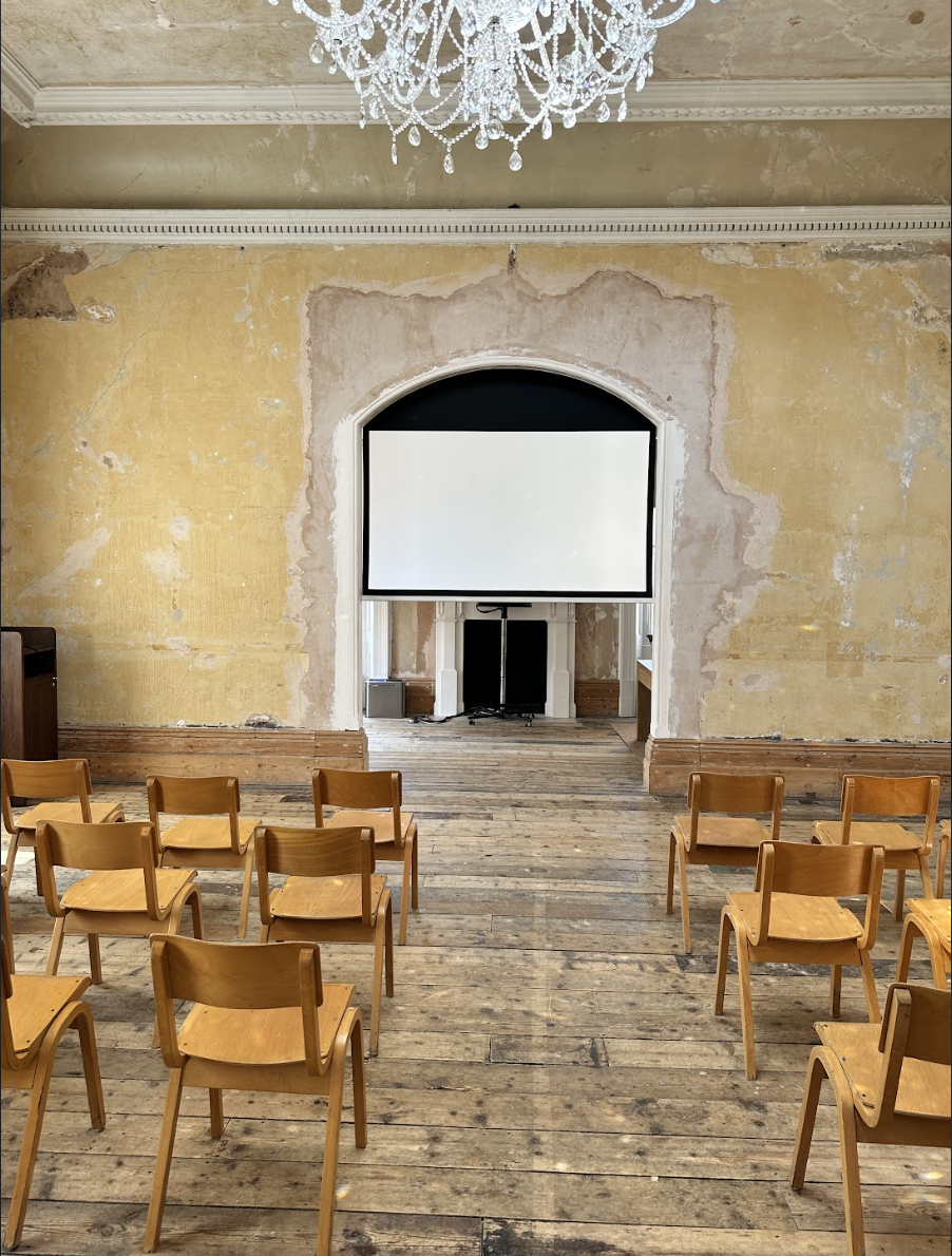 Versatile Knotel Workclub event space with wooden chairs and projection screen for workshops.