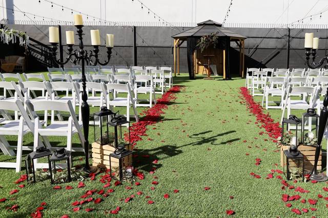 Outdoor wedding ceremony with green grass wall, white chairs, and rose petal aisle.