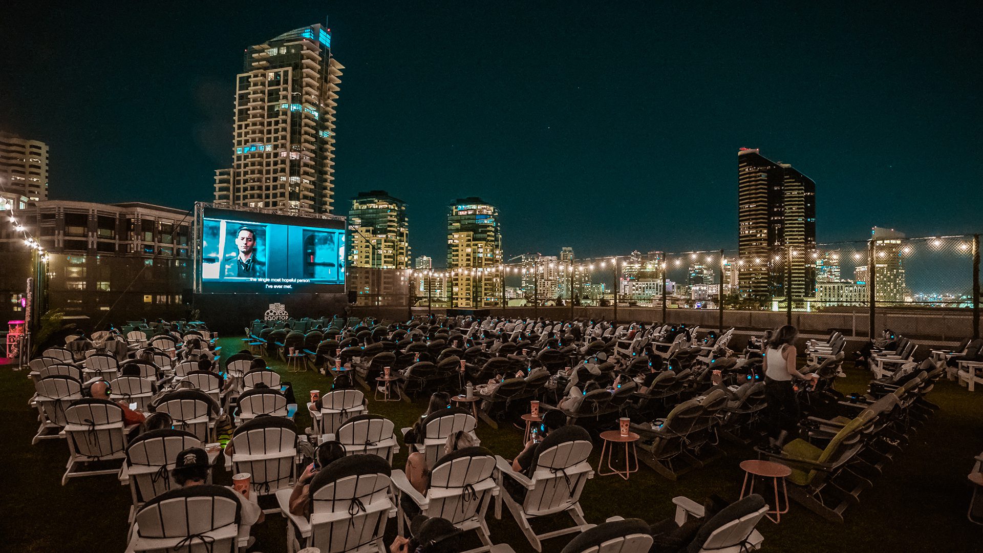 Outdoor movie screening with lounge chairs and city skyline at Rooftop Cinema Club.
