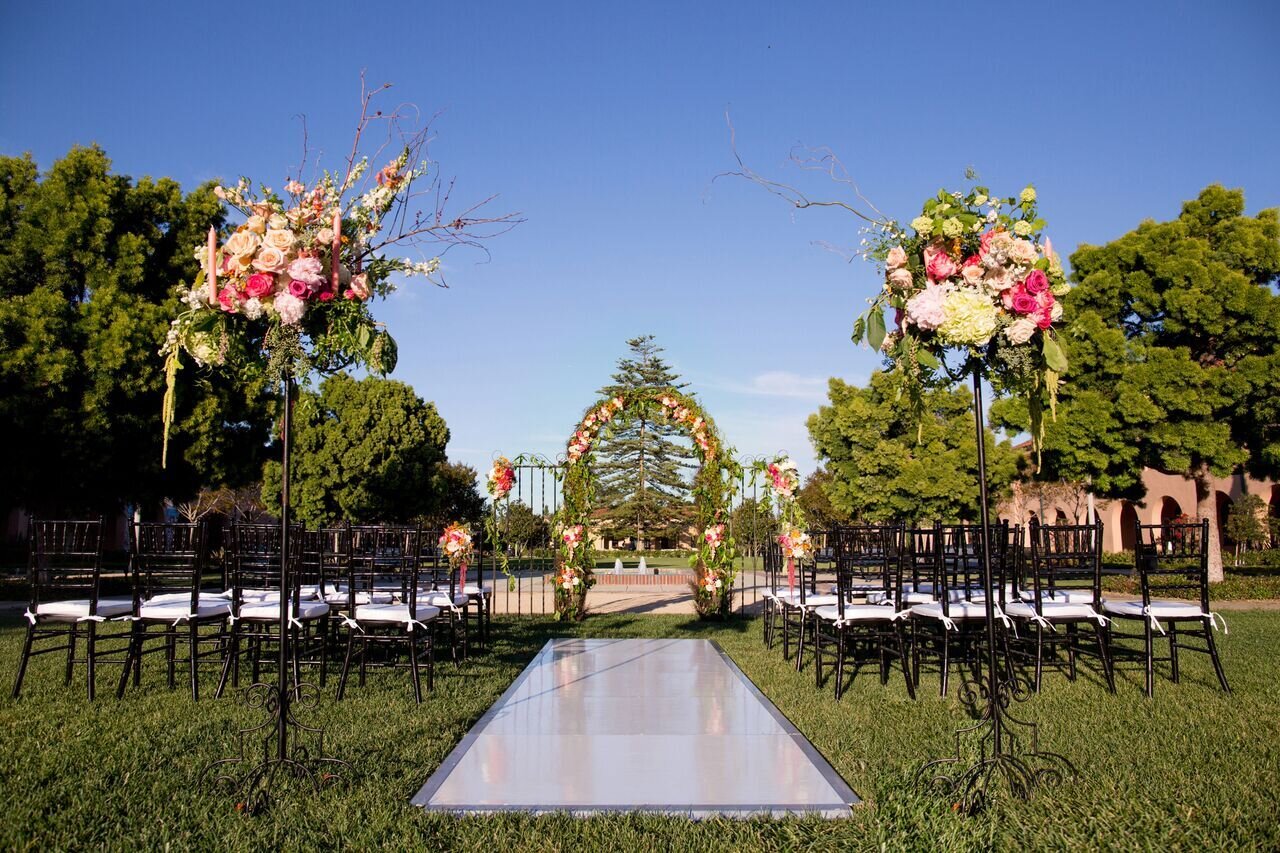 Outdoor wedding ceremony at Liberty Station with floral arch and elegant black chairs.