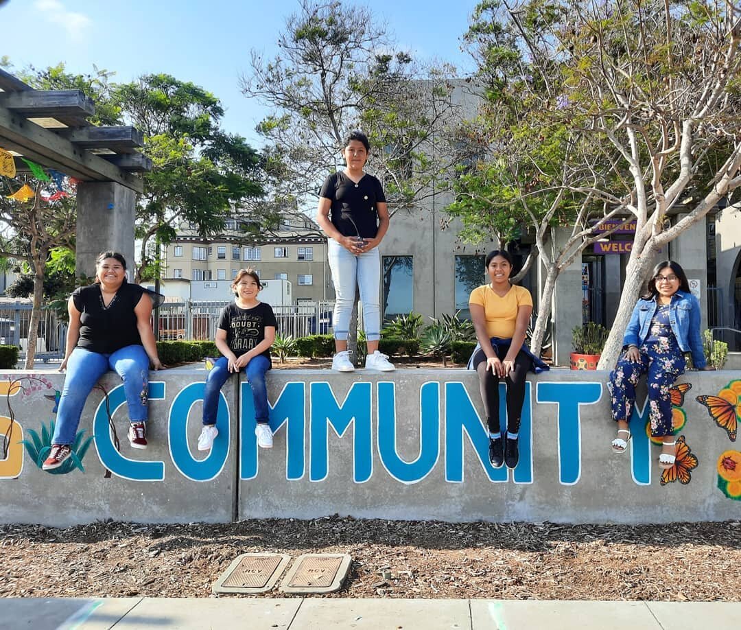 Group posing in front of vibrant "Community" mural at Sherman Heights event venue.