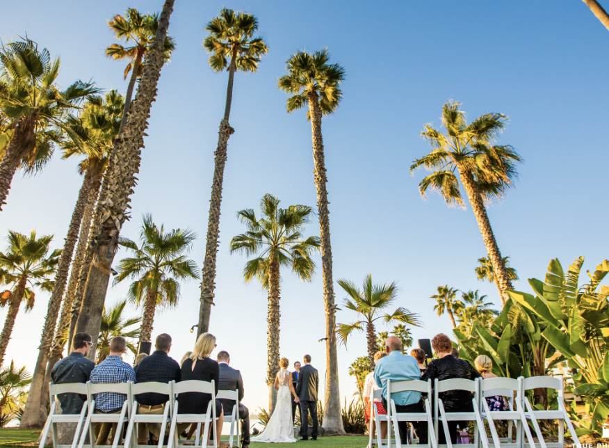 Outdoor wedding ceremony at Island Point Lawn with palm trees and blue sky.