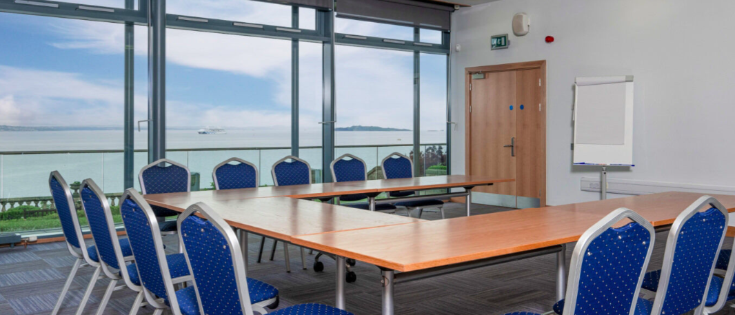 Meeting room N°17 with large table, blue chairs, and coastal view for presentations.