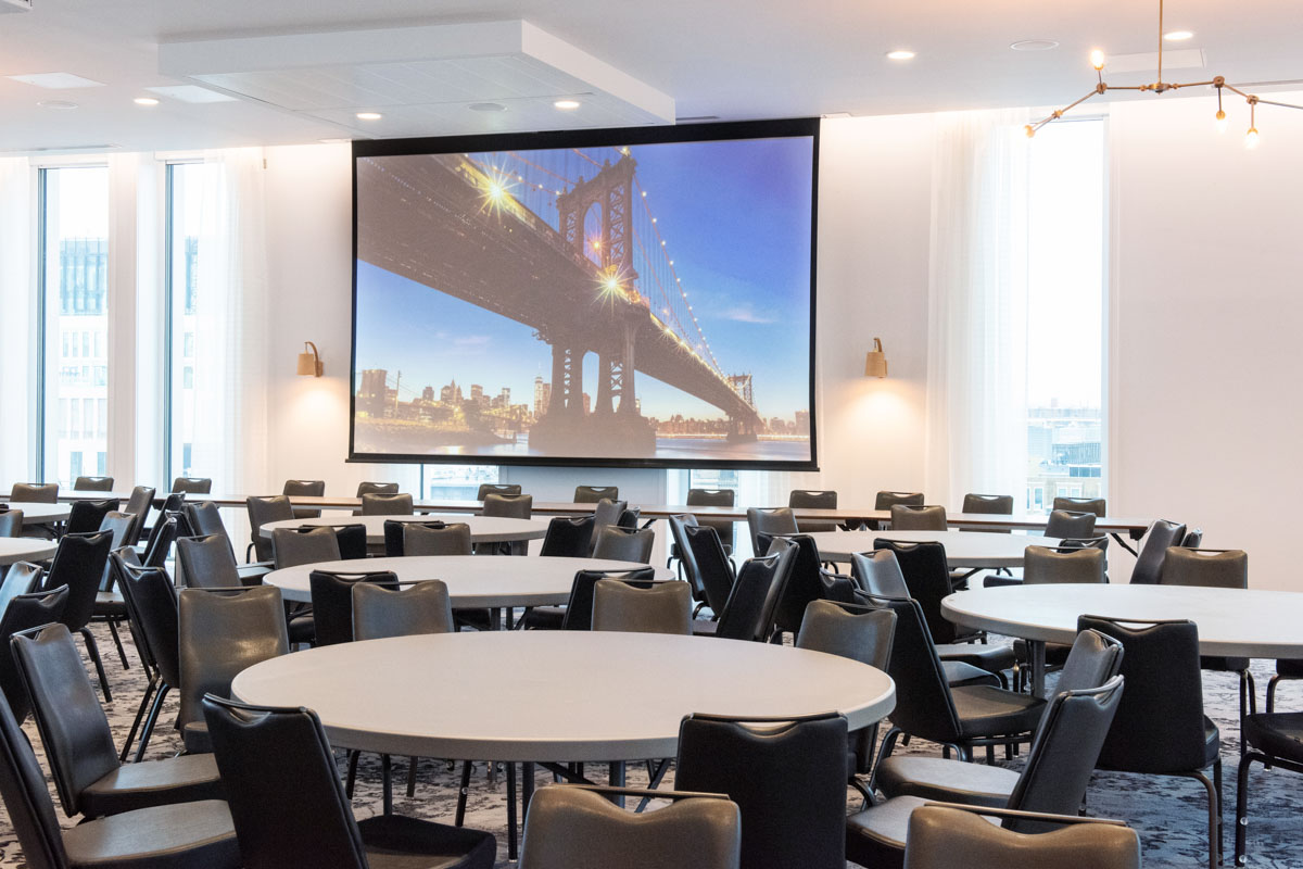 Modern event space in voco Manchester with round tables and Brooklyn Bridge backdrop.