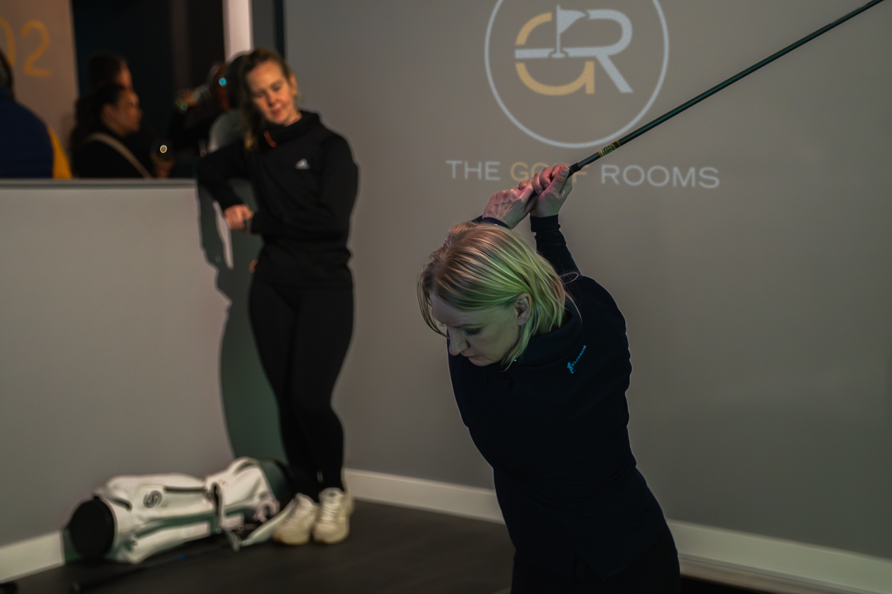 Indoor golf simulator event with participant practicing swing in modern corporate space.