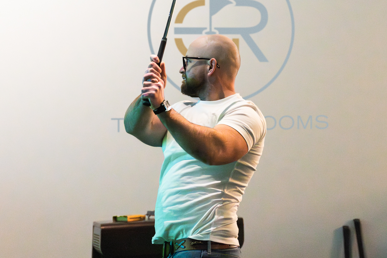 Indoor golf simulator event with engaging speaker using a golf club for team-building workshop.